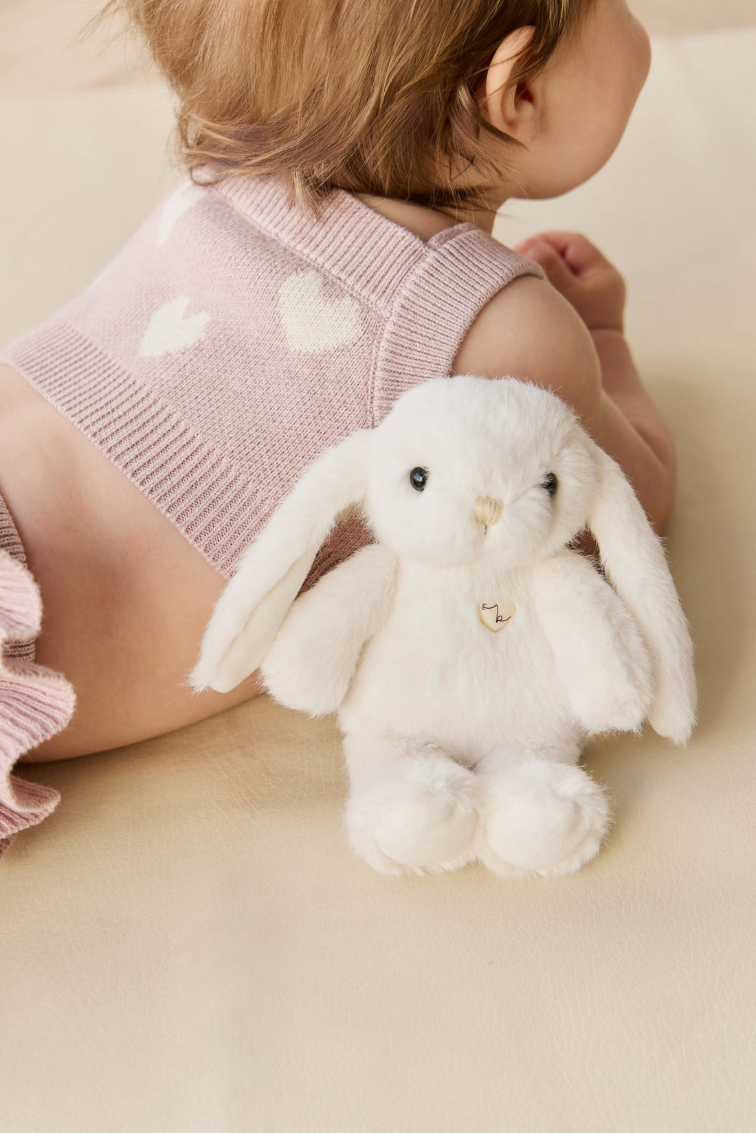 Infant in pink knit outfit with white heart pattern next to a white stuffed bunny.