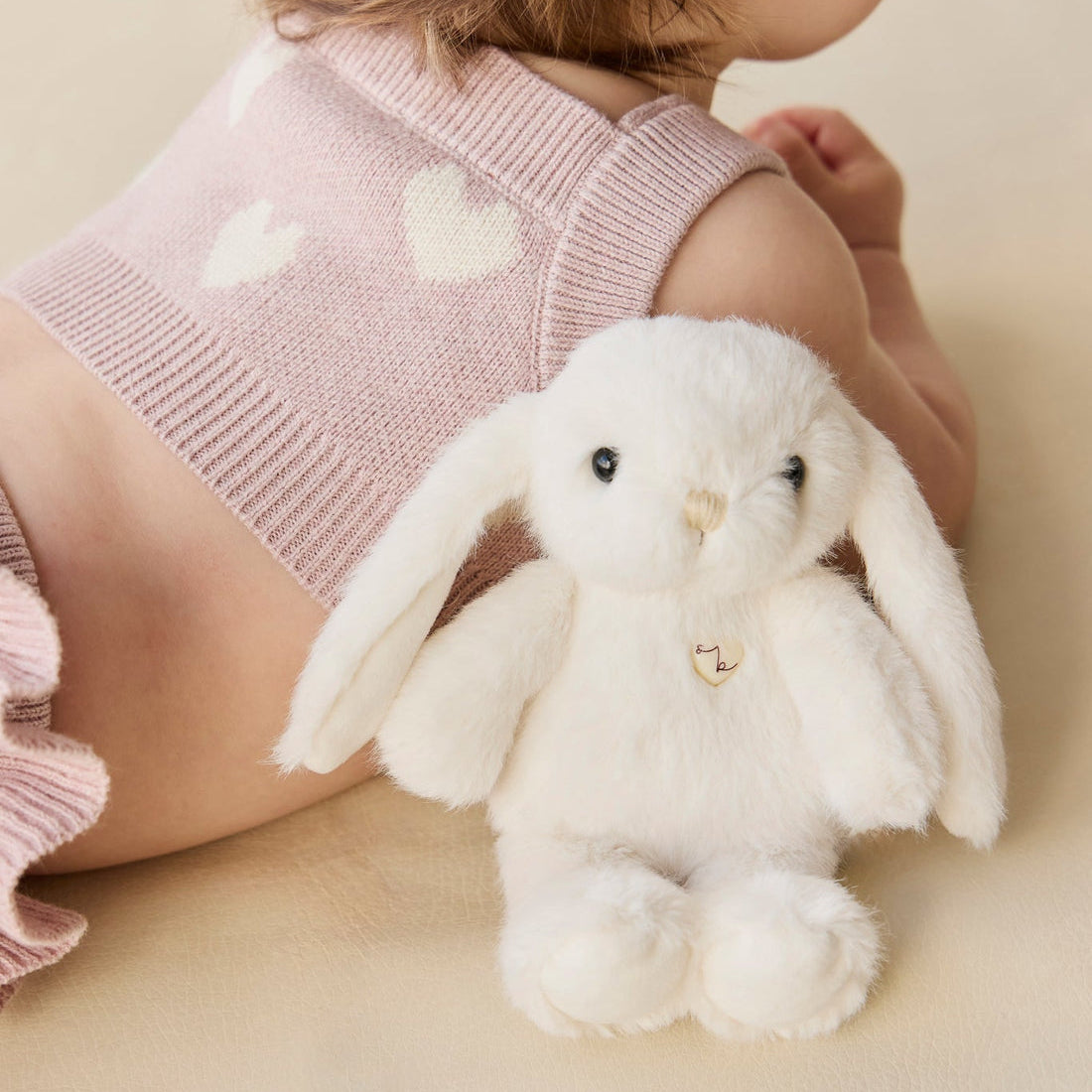 Infant in pink knit outfit with white heart pattern next to a white stuffed bunny.