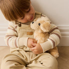 Child in striped sweater and tan overalls, hugging a plush dog.