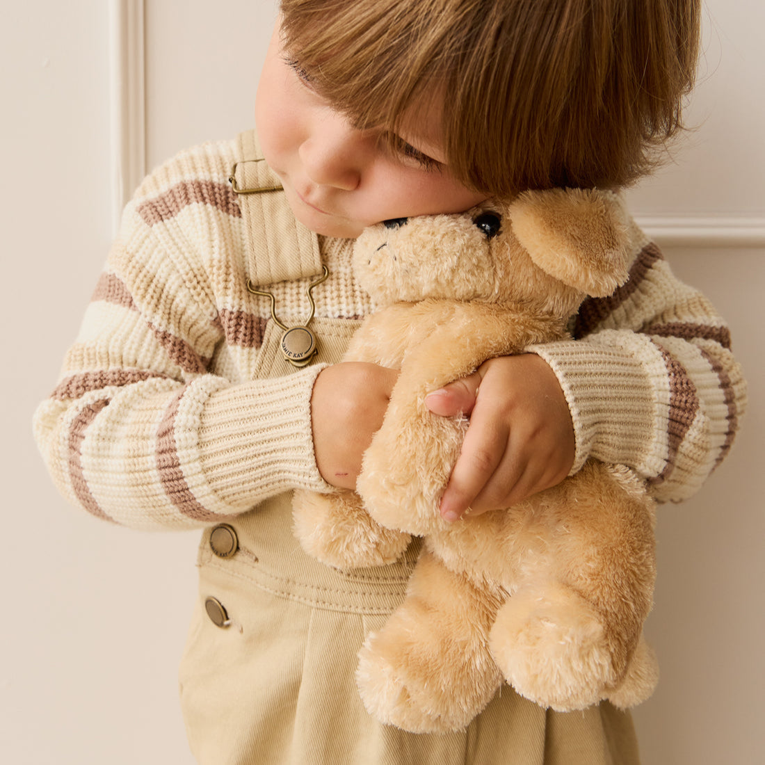 Child hugging plush puppy toy. Striped sweater and overalls.