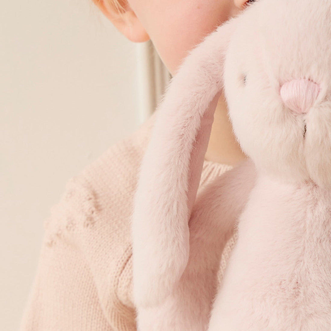 Child holding a pink stuffed bunny, wearing a pink sweater.