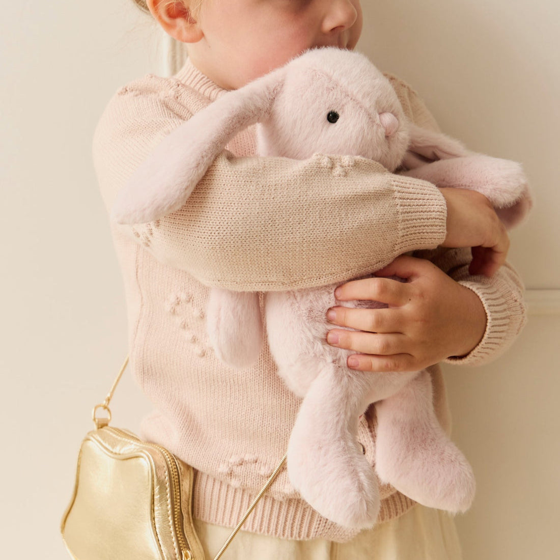 Young girl hugging a pink plush bunny while wearing a pink sweater and gold purse.