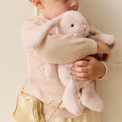 Young girl hugging a pink plush bunny while wearing a pink sweater and gold purse.