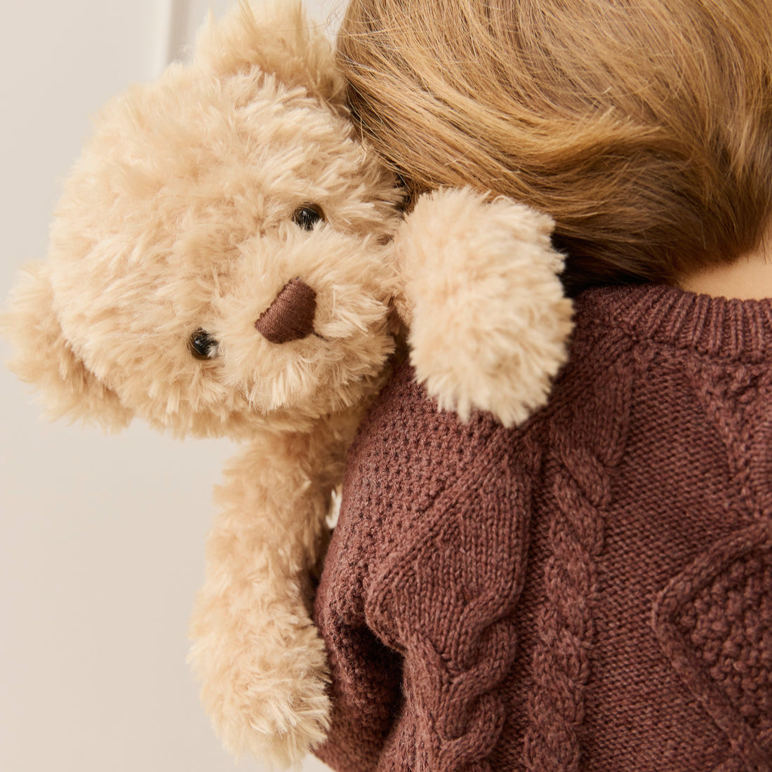 Child in brown cable knit sweater hugging a tan teddy bear.