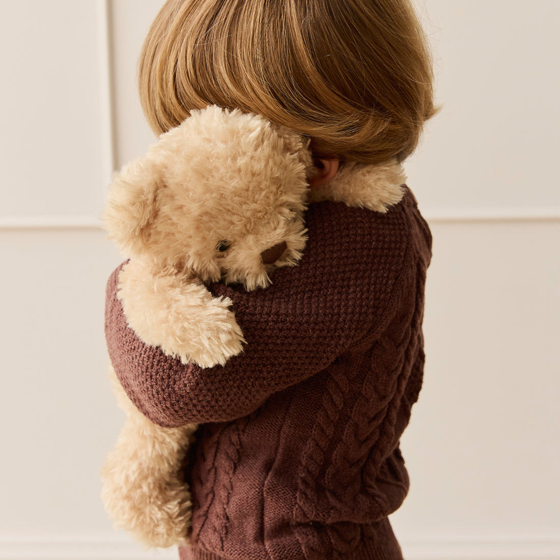Child in brown knit sweater hugging a teddy bear.