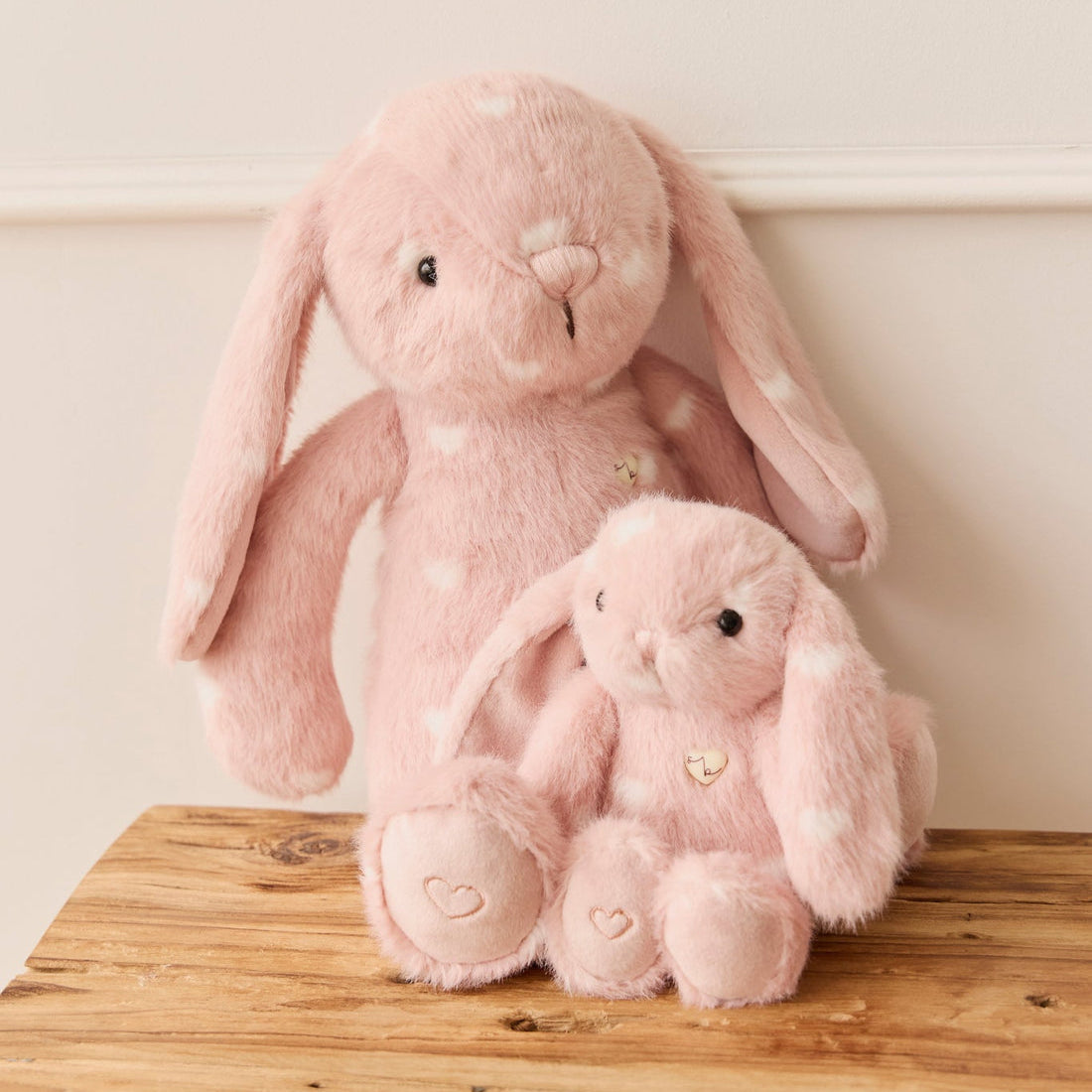 Two pink stuffed bunny toys with white hearts on a wooden surface.