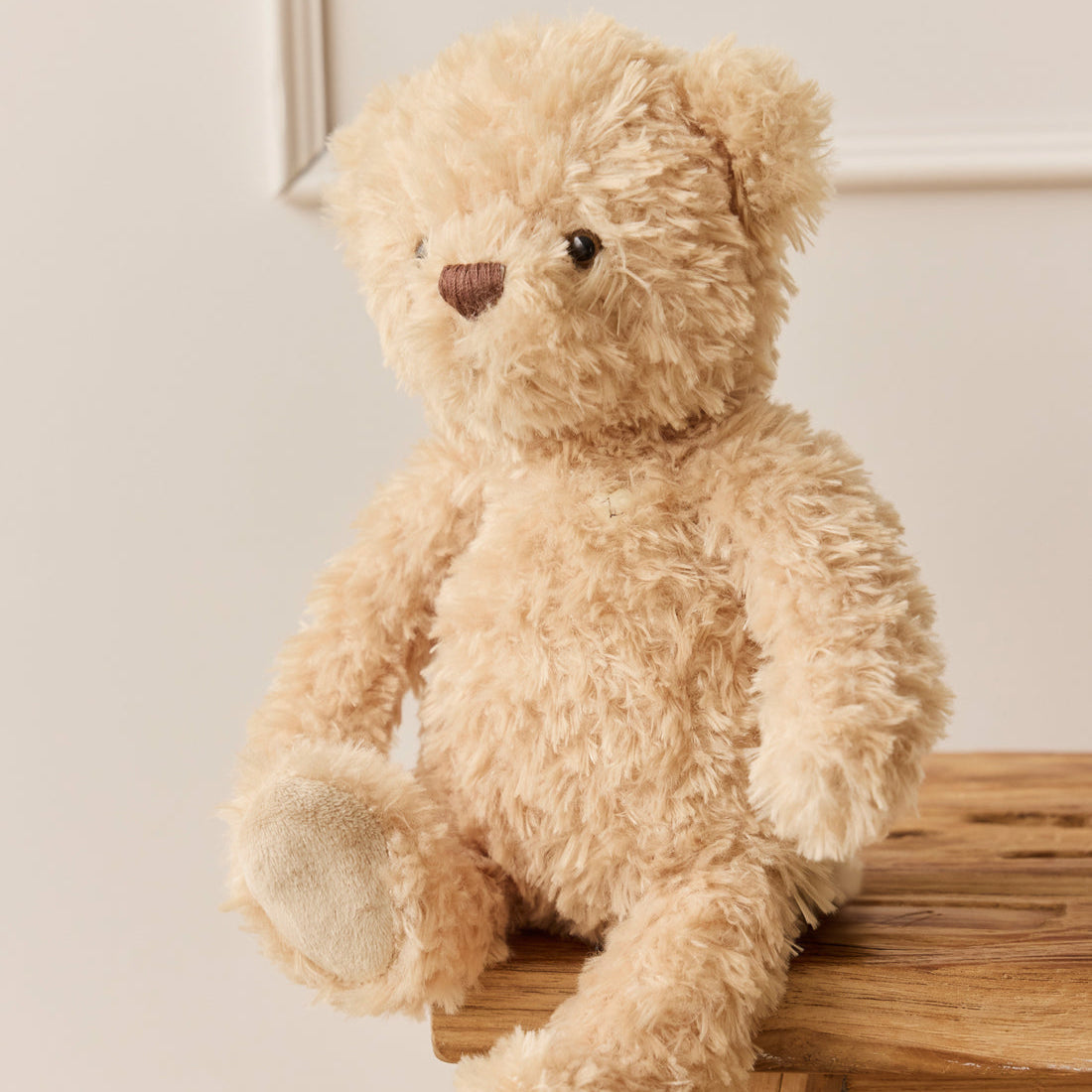 Light brown teddy bear sitting on wooden surface.