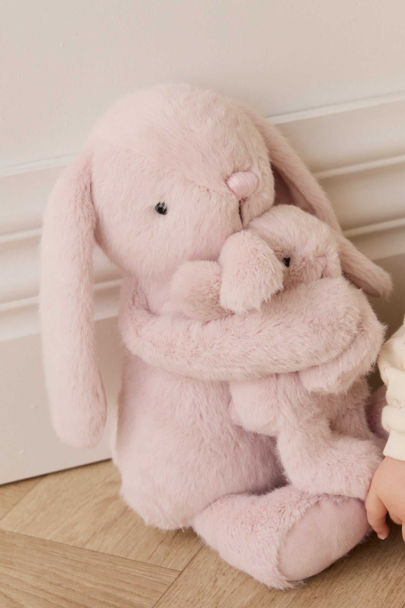 A light pink plush rabbit embracing a smaller plush rabbit.