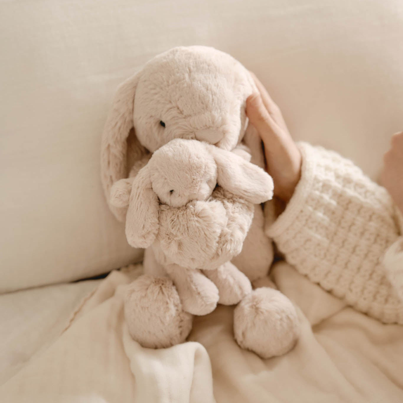 Two plush bunny toys on a soft surface with a hand holding one of them.