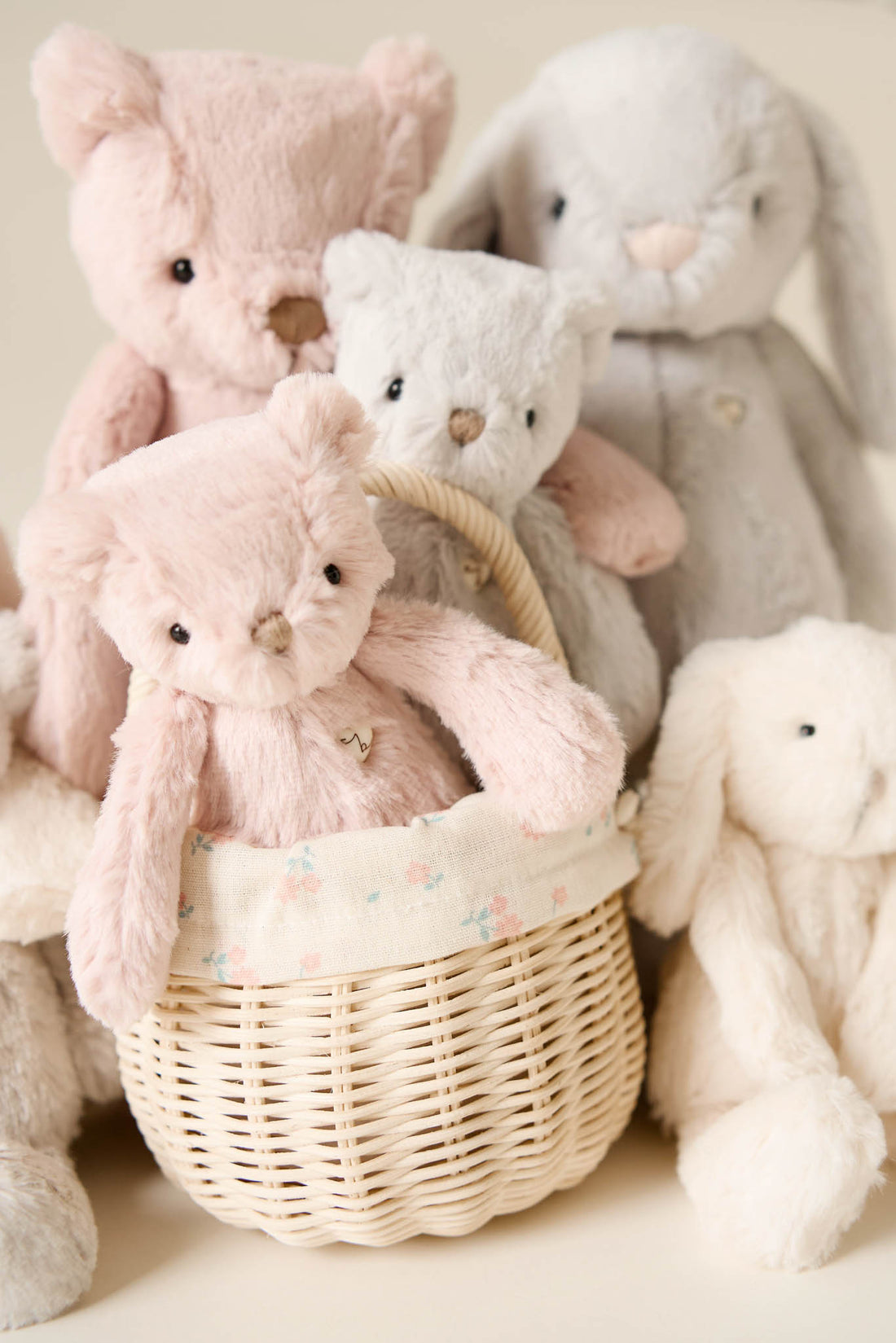 Several plush teddy bears and bunnies are arranged with a pink teddy bear in a wicker basket.