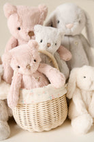 A collection of stuffed teddy bears and bunnies, with one pink bear in a woven basket with a floral liner.