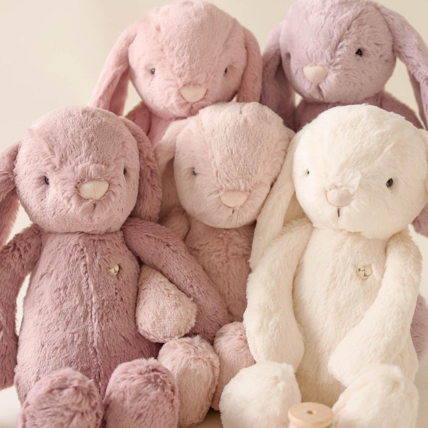 Five plush bunny toys in pastel pink, lavender, and white hues, grouped together with a spool of ribbon.