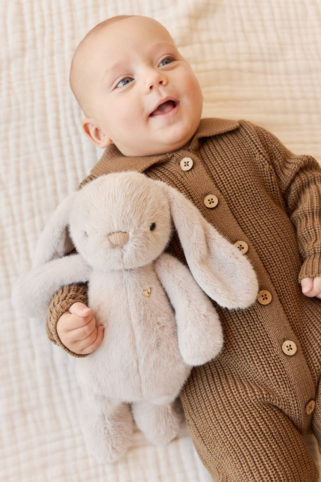 Baby in brown knit romper with stuffed bunny.