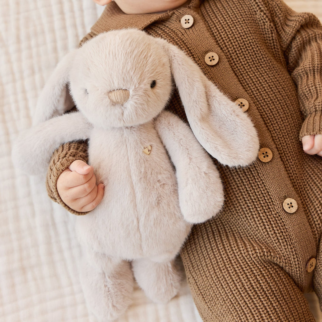 Baby in brown knit romper with stuffed bunny.