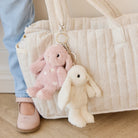 Child in blue jeans and pink shoe standing next to a tote bag with two plush bunny keychain.