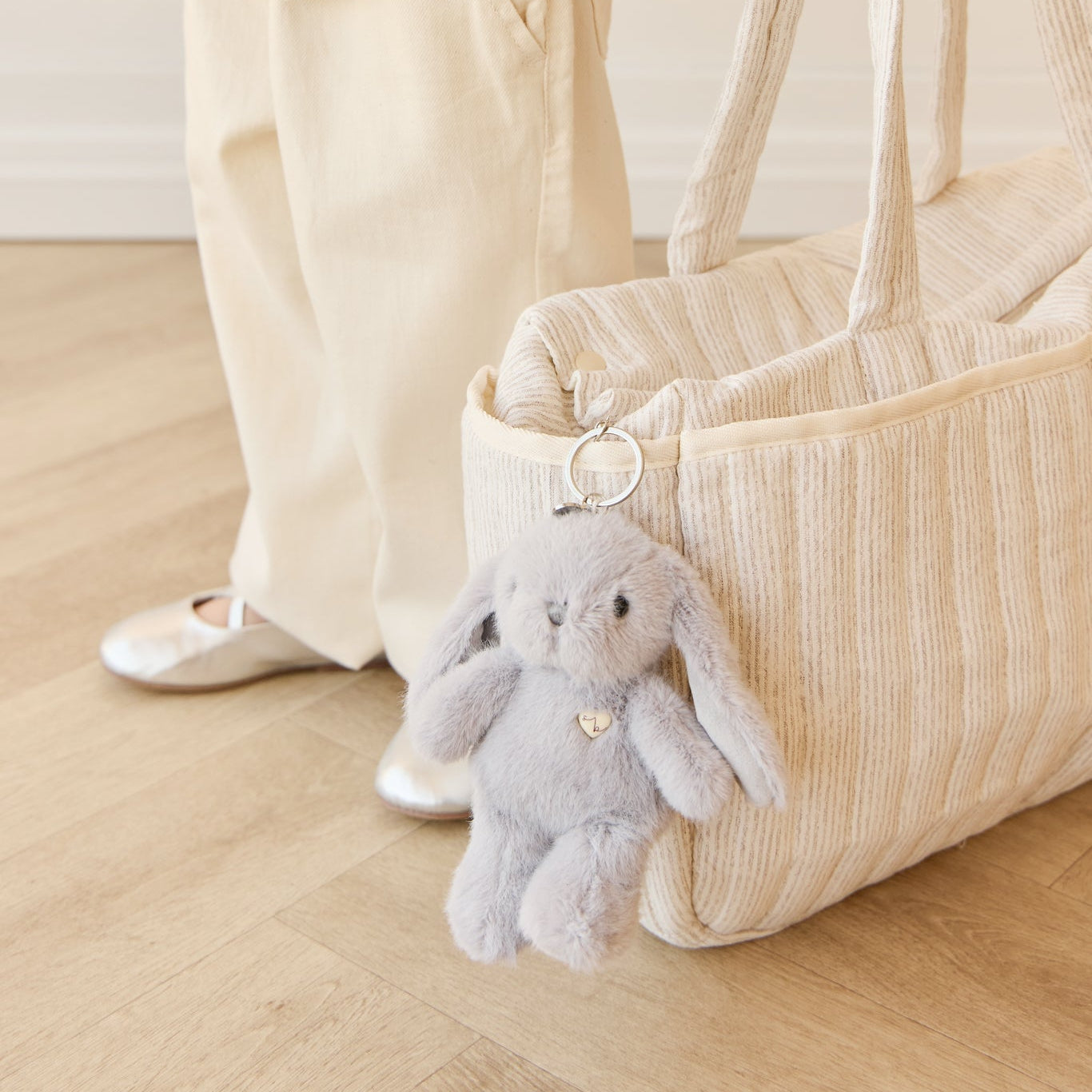 A child wearing a denim jacket and beige pants holding a striped tote bag with a plush bunny keychain.