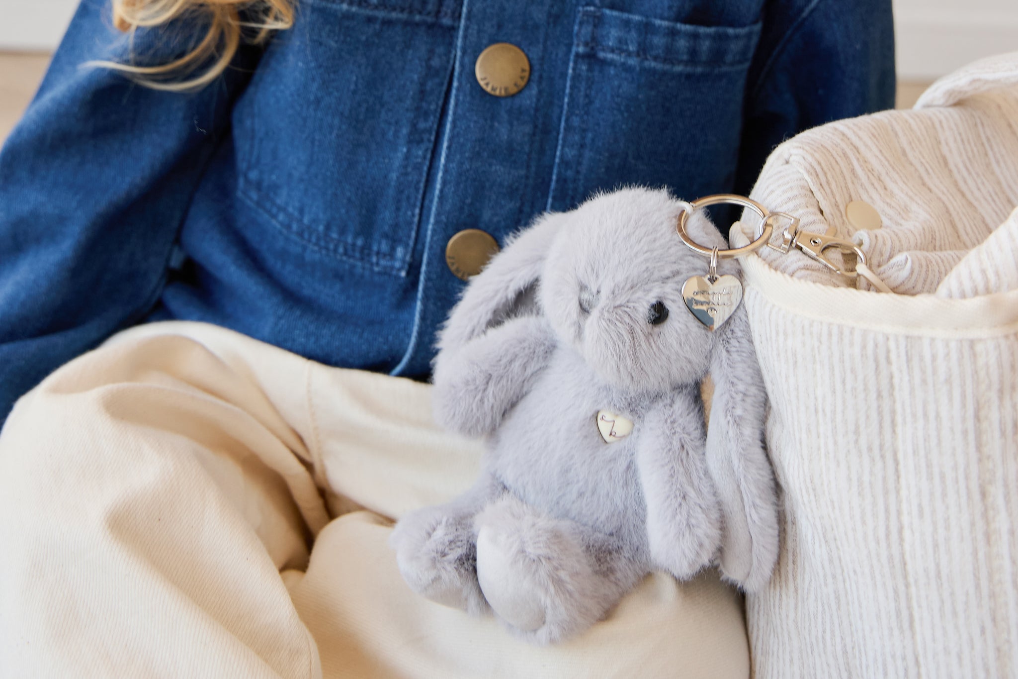 Blue denim jacket, off-white pants, gray plush bunny keychain, striped knit bag.