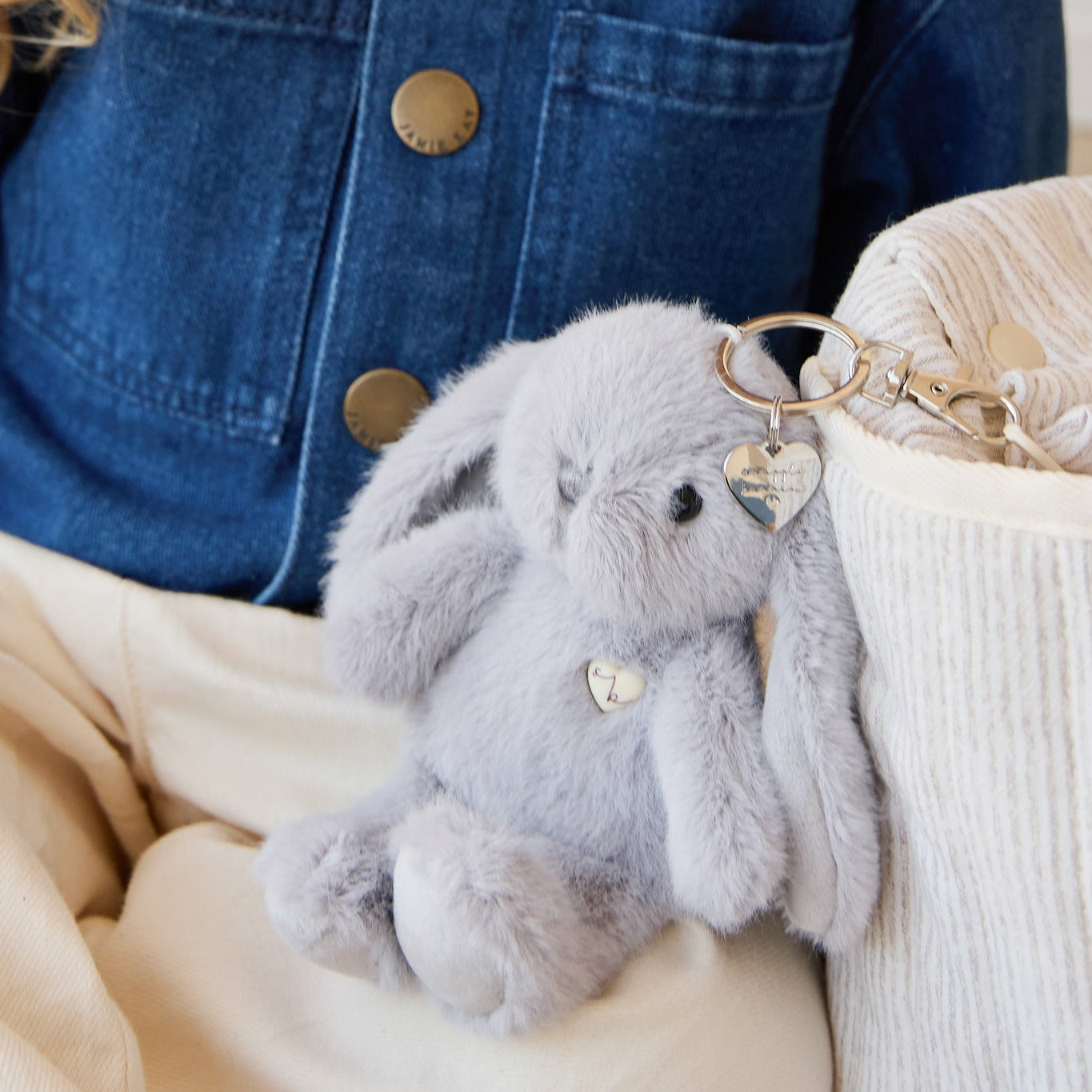 Blue denim jacket, off-white pants, gray plush bunny keychain, striped knit bag.
