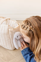 Little girl snuggling with a stuffed bunny attached to a light beige bag.