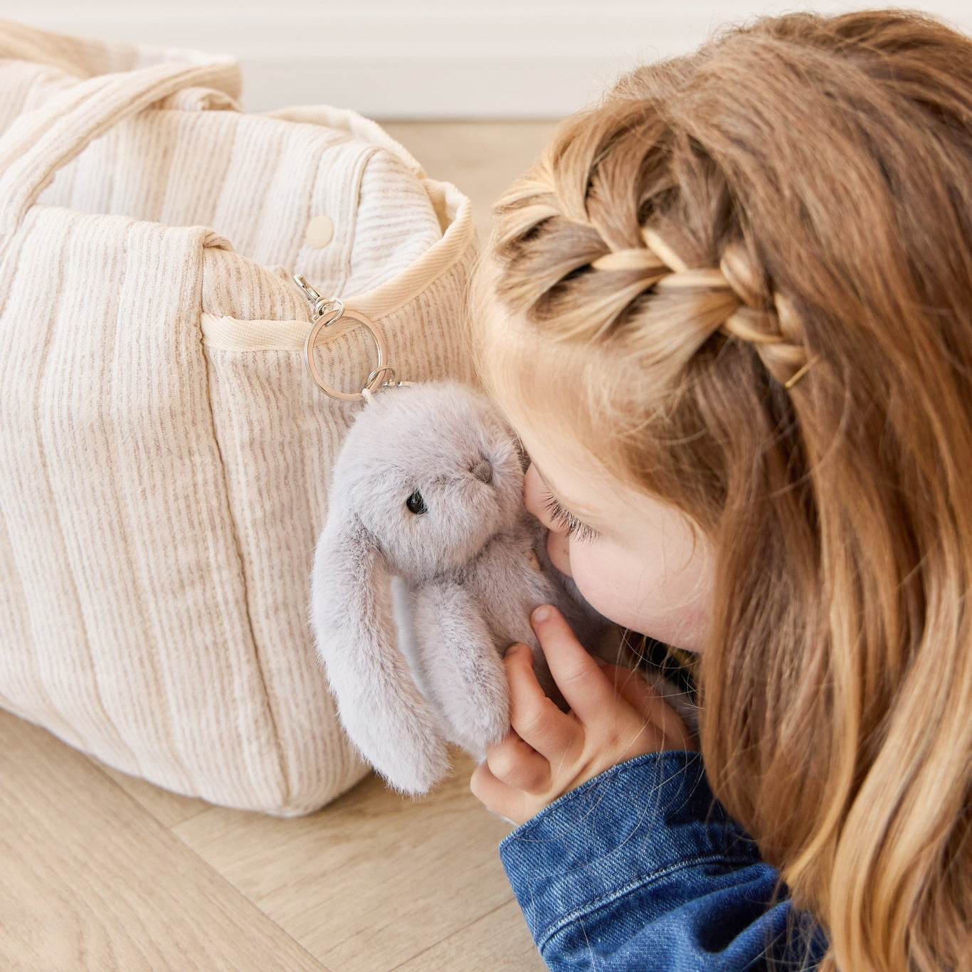 Little girl snuggling with a stuffed bunny attached to a light beige bag.