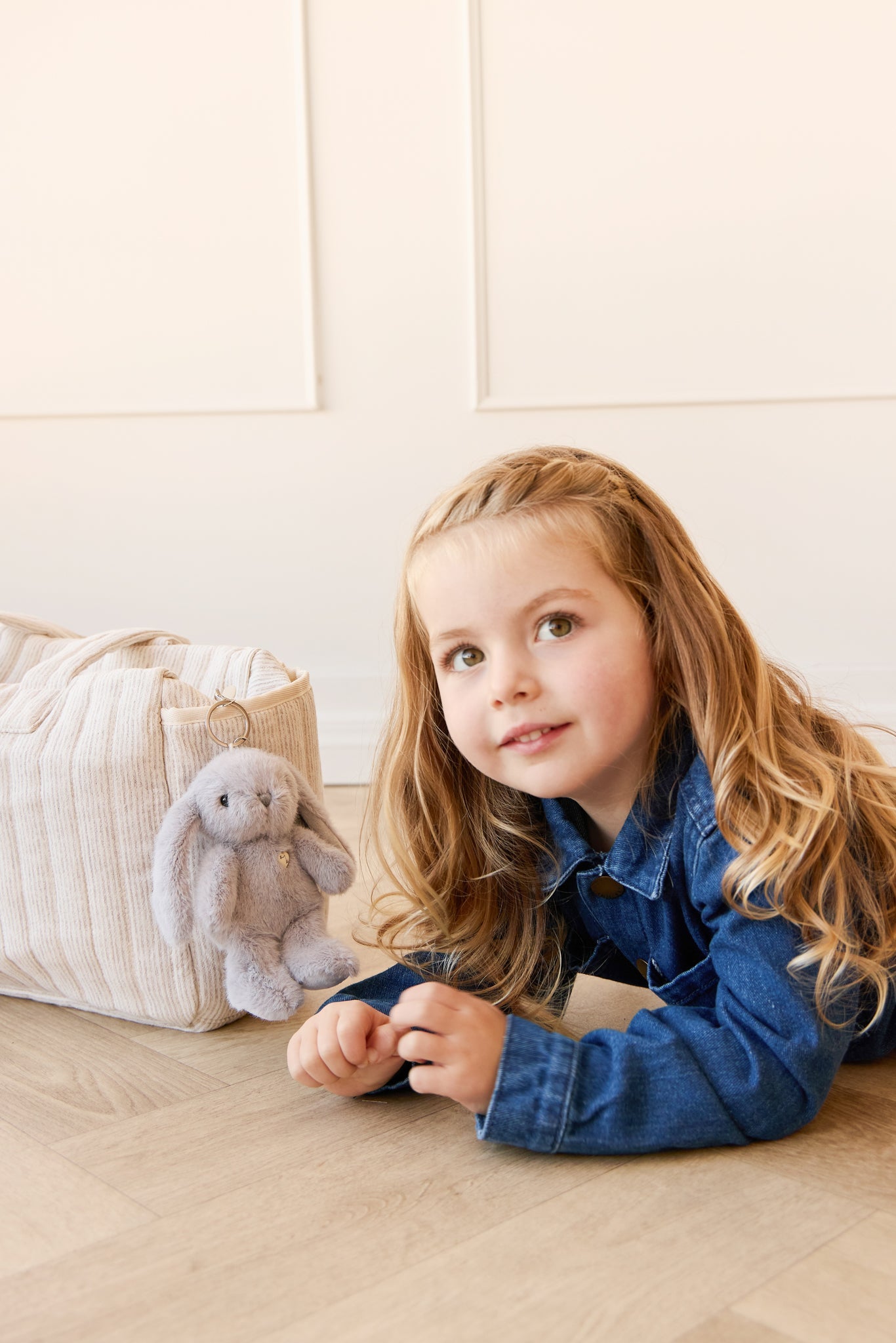 A young girl in a denim jacket poses with a plush bunny and a cream-colored corduroy bag.