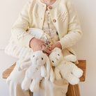 Young person in off-white outfit seated, holding plush bunny and bear keychains.