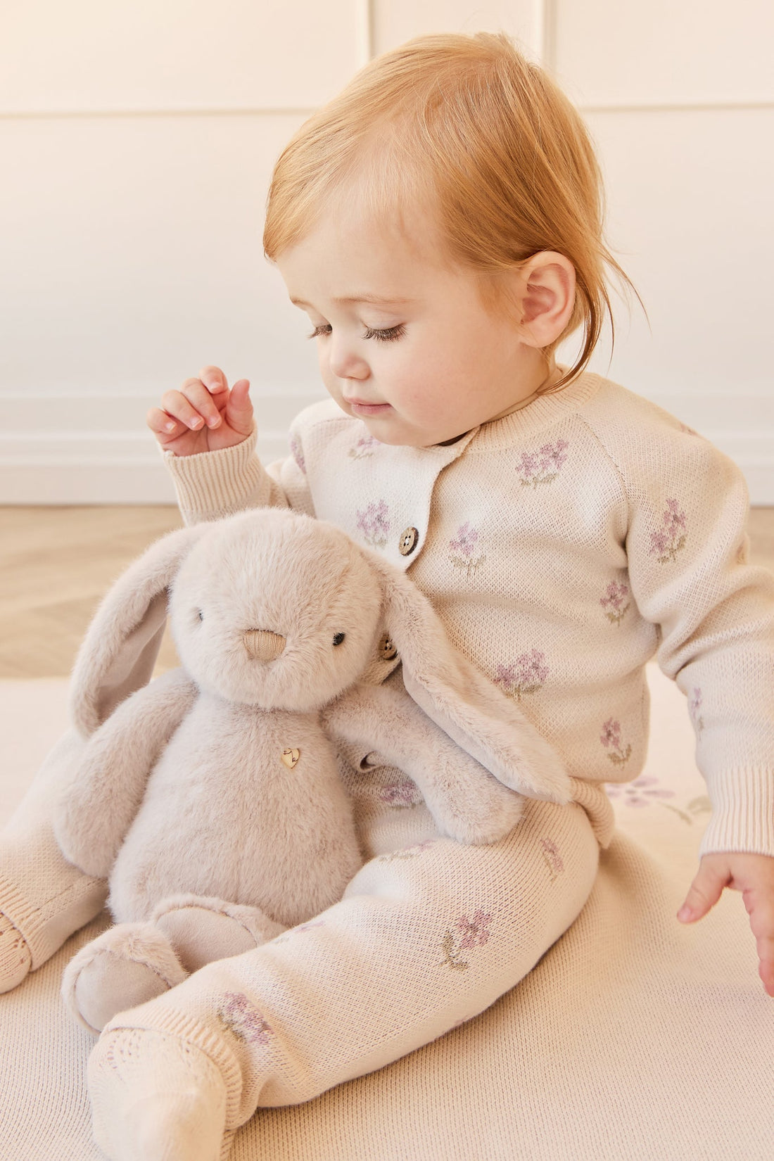 Infant with bunny plush, wearing matching knitwear with floral embroidery.