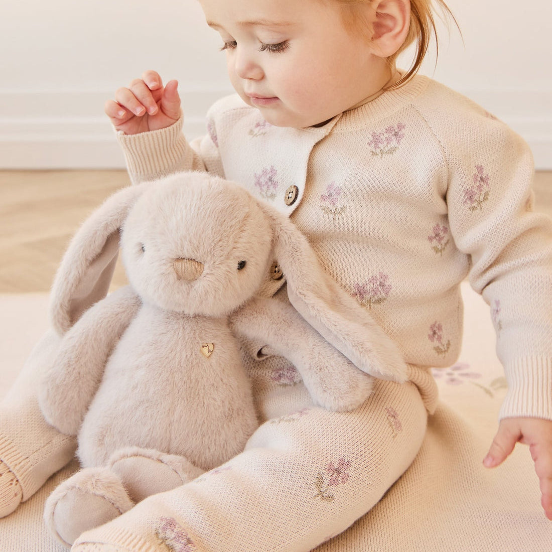 Infant with bunny plush, wearing matching knitwear with floral embroidery.