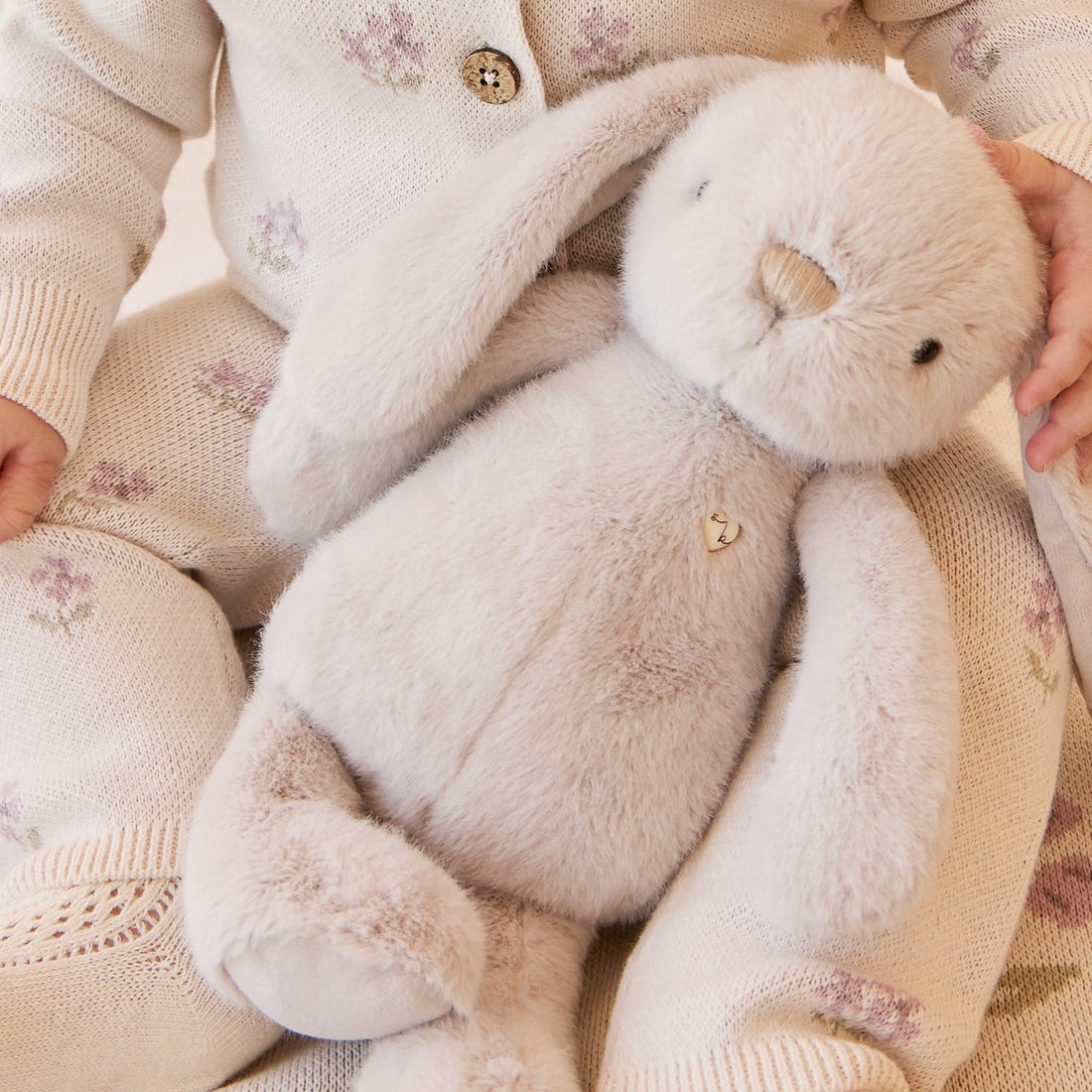 Infant in floral knitwear holding a plush bunny.