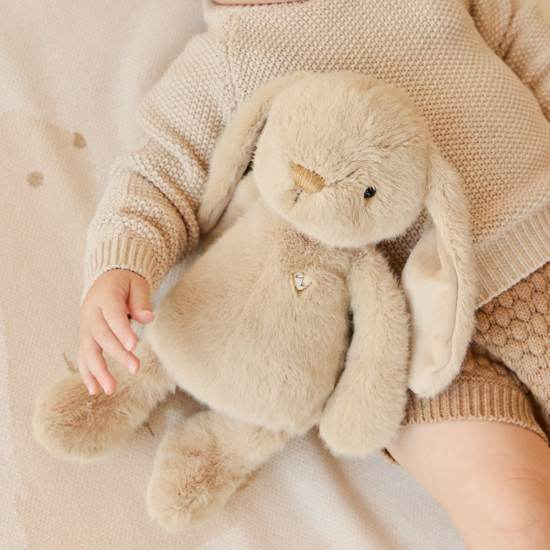 Child in knit sweater holds a plush bunny toy.
