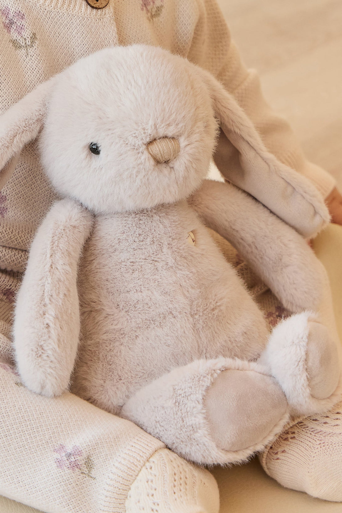 Stuffed bunny toy with beige fur in child's lap, wearing light sweater and patterned leggings.