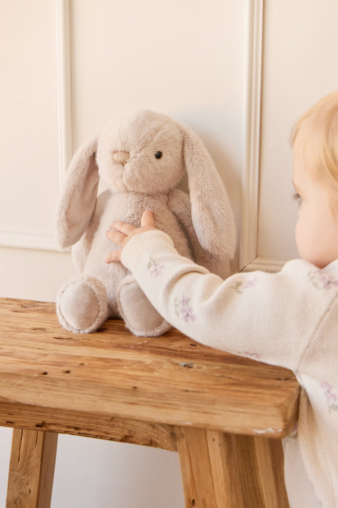 Stuffed bunny on wooden bench with child's hand reaching.