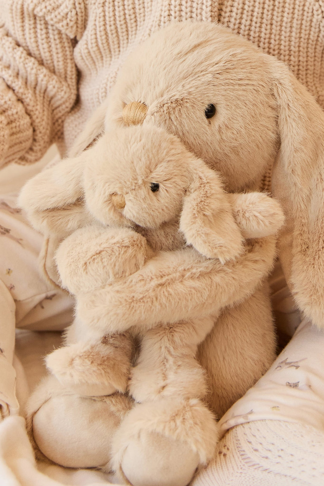 Two stuffed rabbits hugging, light brown fur, soft textures.