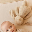 Baby in sweater and a beige plush bunny on a beige surface.