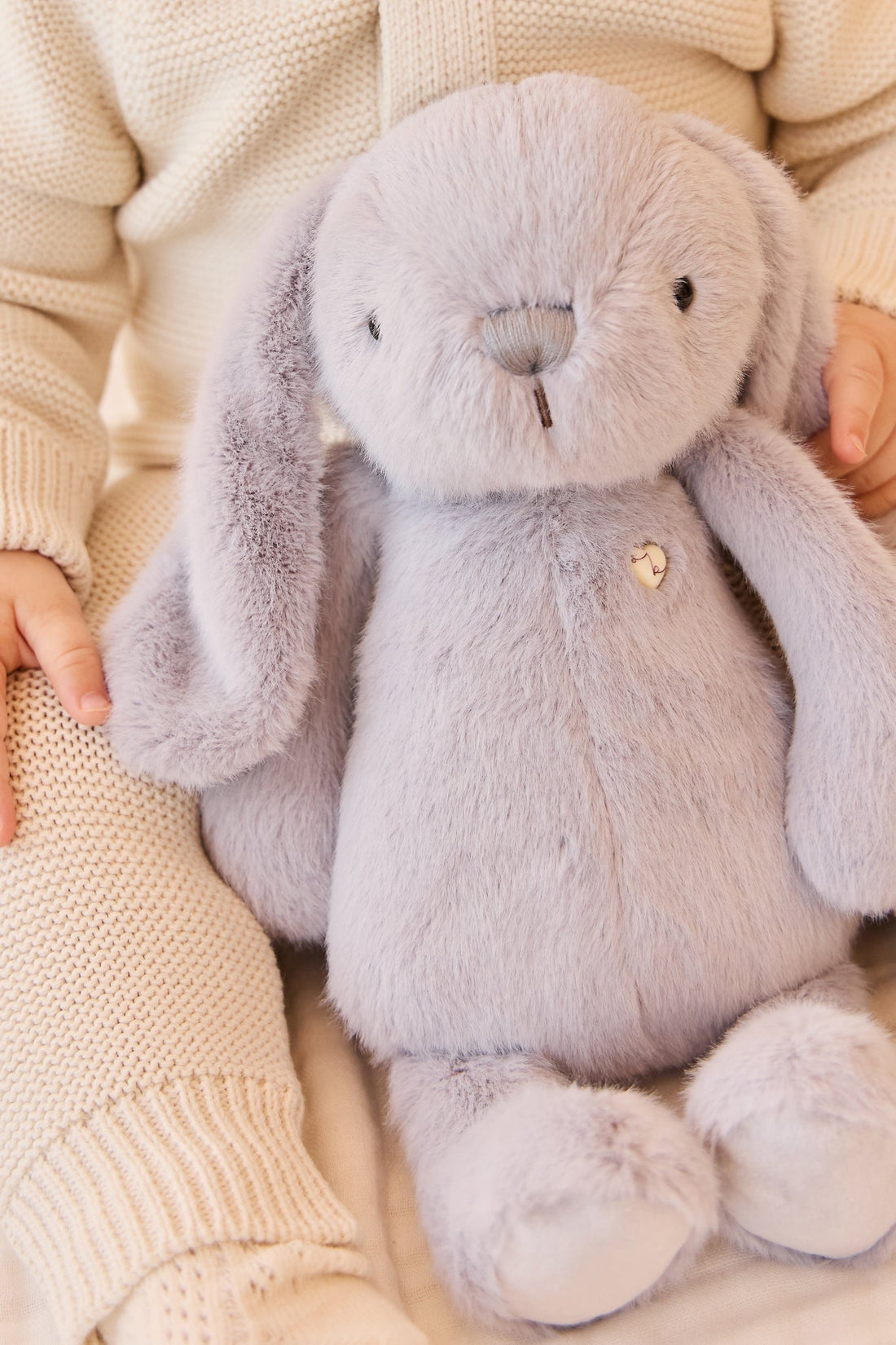 Baby holding gray plush bunny toy.