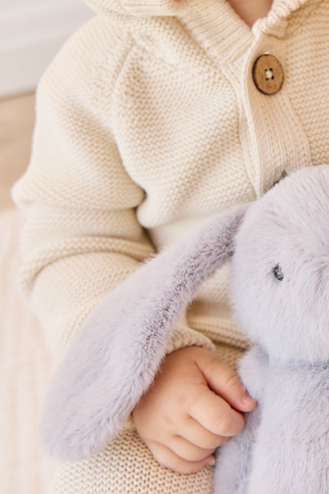 Child in knitted cardigan holding a plush bunny.