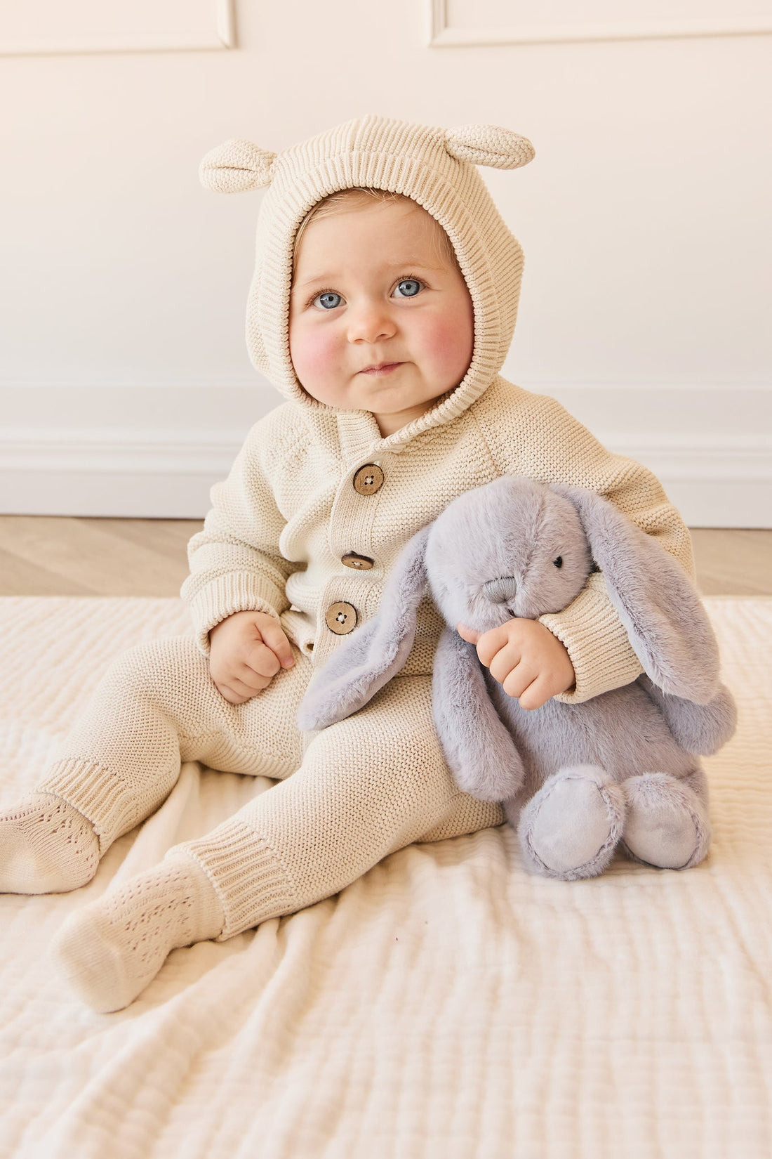 Baby in cream knit outfit with bunny plush toy.