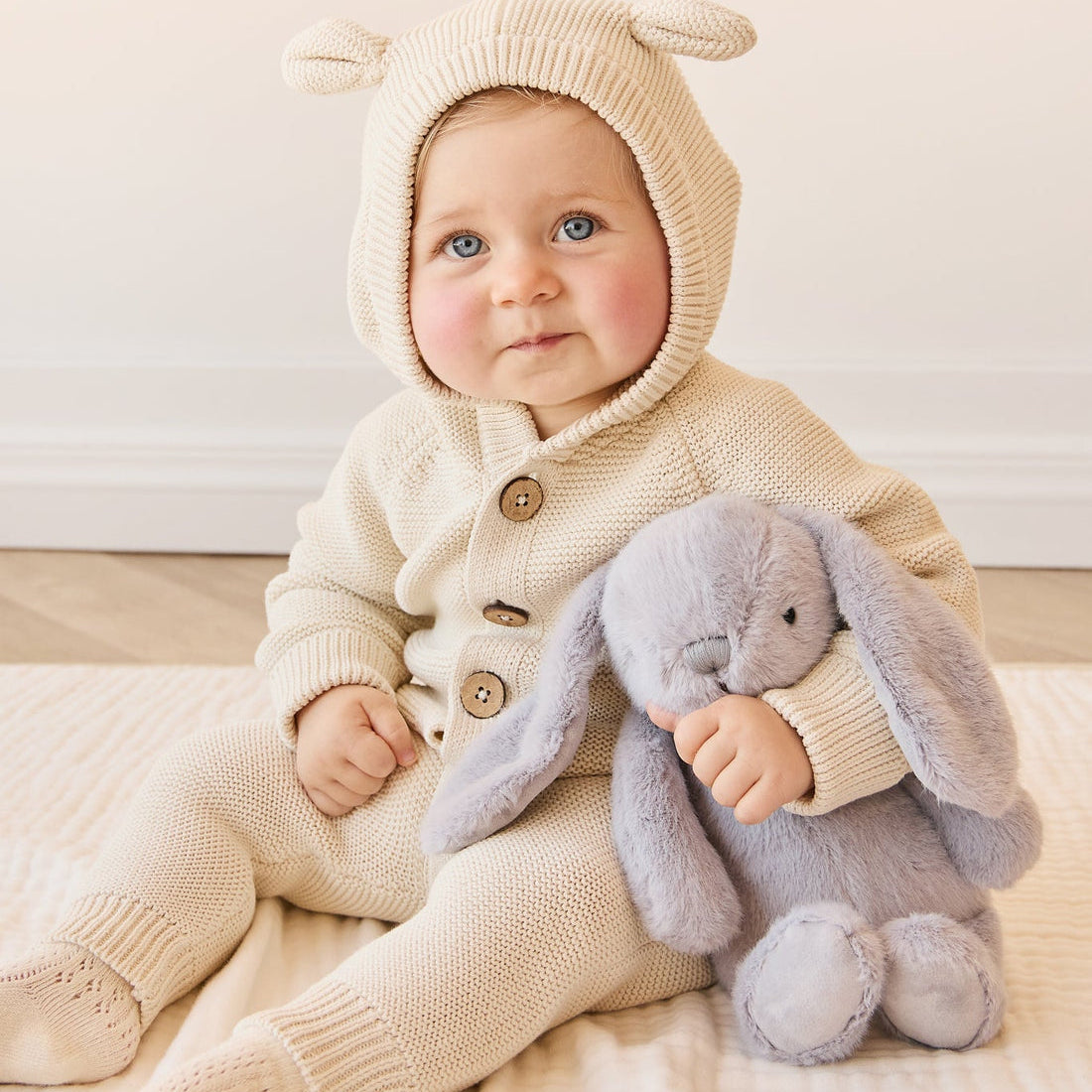 Baby in cream knit outfit with bunny plush toy.