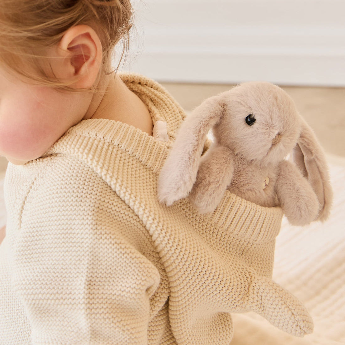 A child wearing a cream-colored knit sweater holding a plush bunny.
