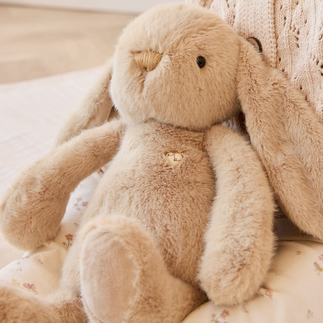 Tan plush bunny with embroidered heart on floral fabric.