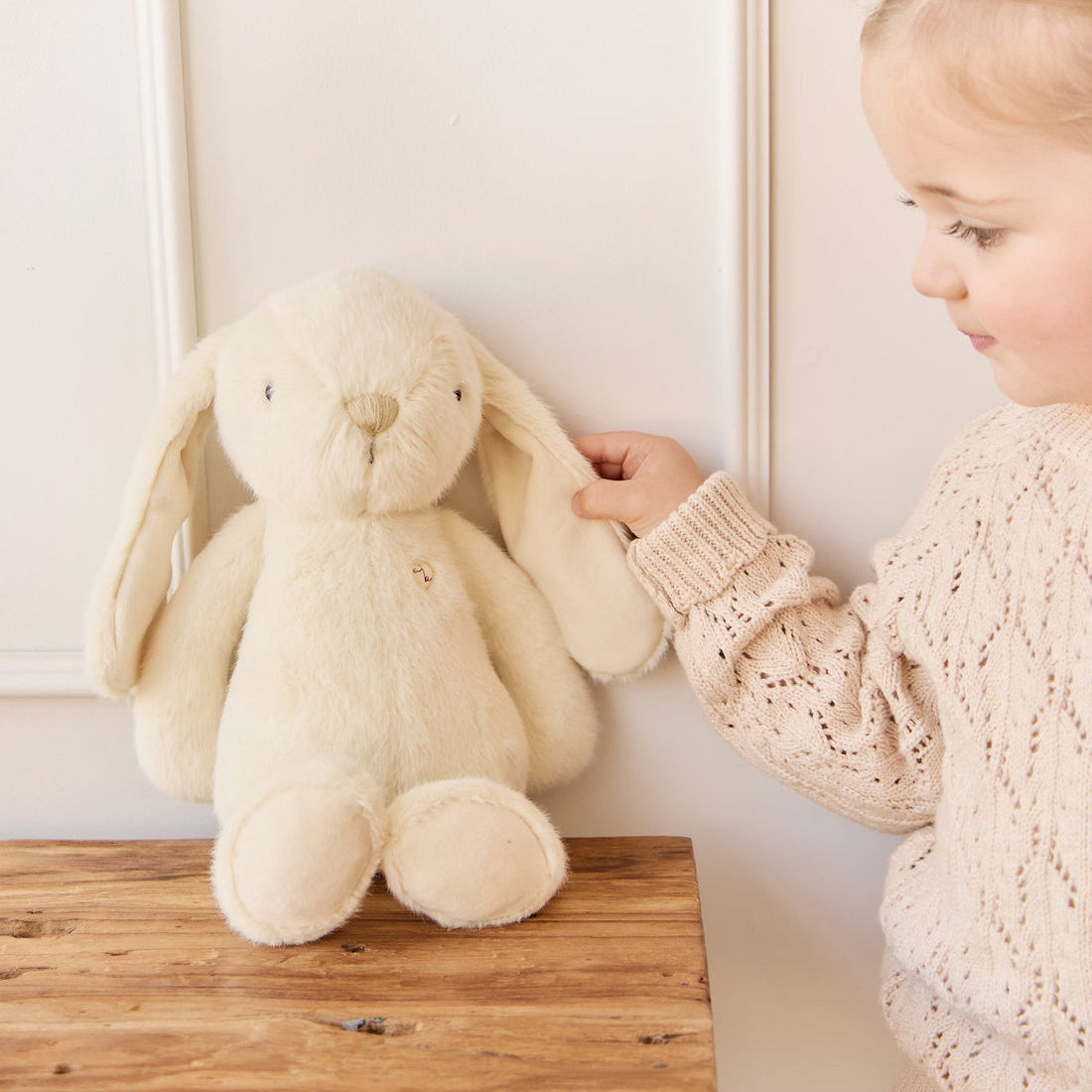 A young girl holds the ear of a white stuffed rabbit toy.