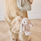 Two plush rabbit keychains hang from a quilted handbag attached to a child's tan pants.