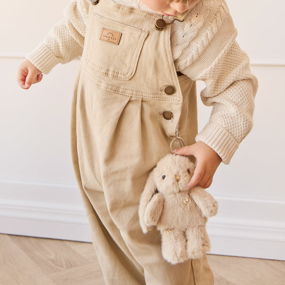 Toddler in beige corduroy overalls and sweater holding a plush bunny.