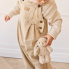 Toddler in beige corduroy overalls and sweater holding a plush bunny.