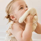 A baby in a beige dress holding a white plush bunny.