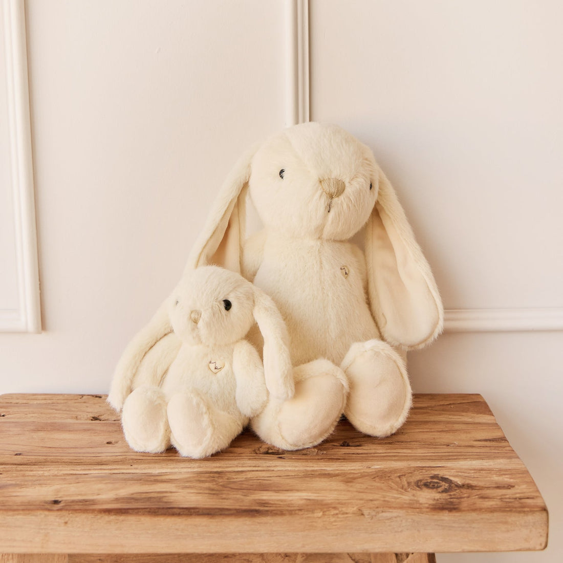 Two stuffed bunny rabbits sitting on a wooden table.