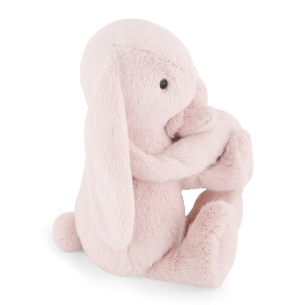 A pink plush bunny with long ears sits and holds its forelegs.