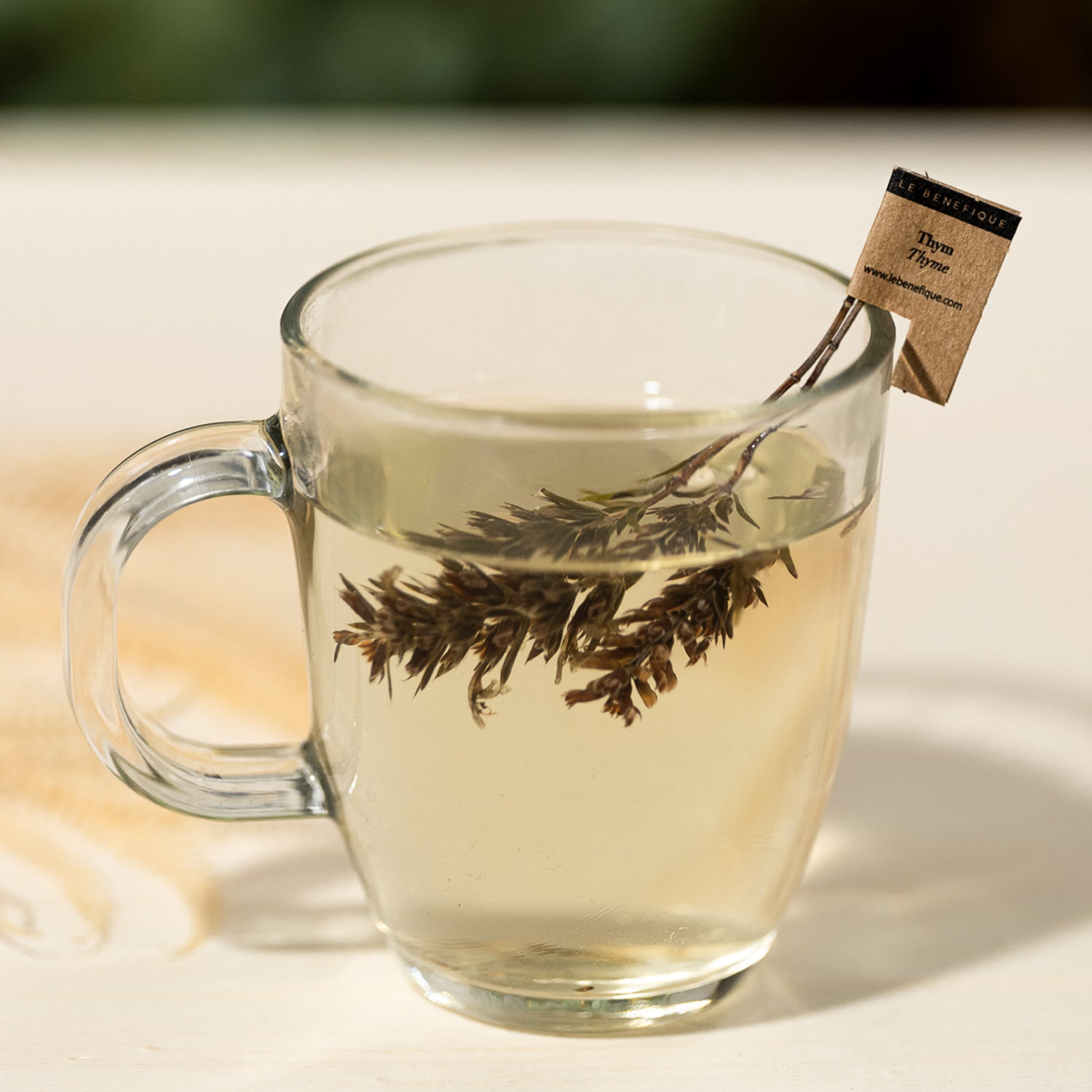 Clear mug of thyme tea with a branded tag.