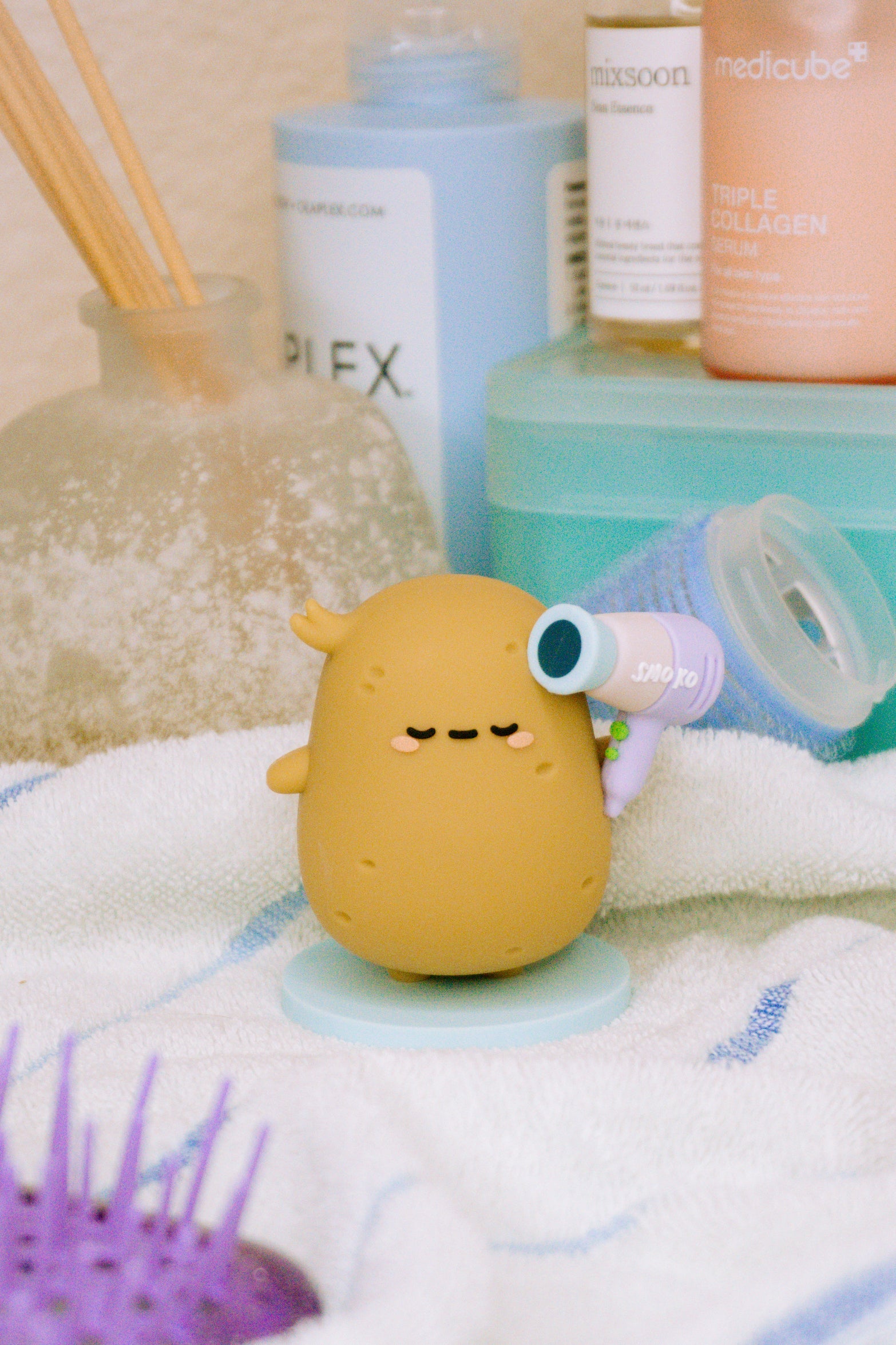 Cartoon potato figure holding a small purple hairdryer on a white towel.