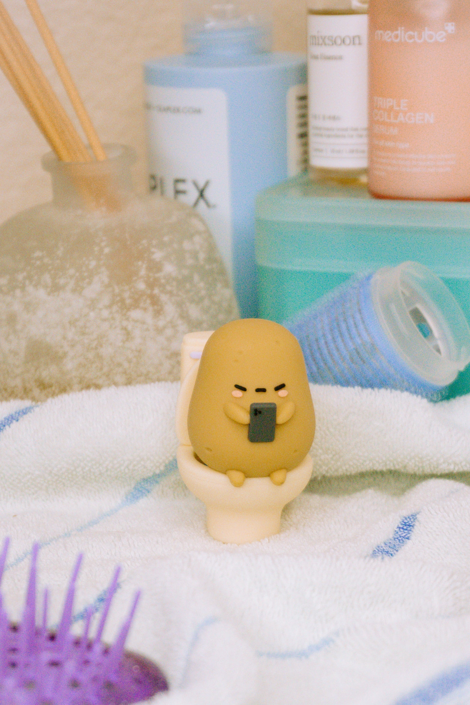 Animated potato figurine on a miniature toilet, holding a phone, on a white and blue towel.